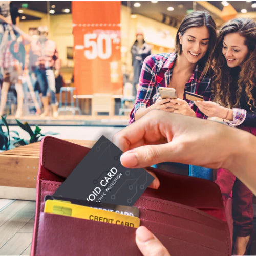 Person holding a wallet with credit cards, two women using smartphones in the background.