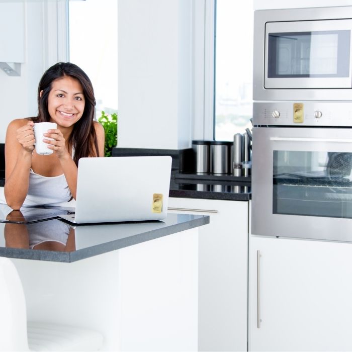 Woman using a laptop in a kitchen holding a mug.